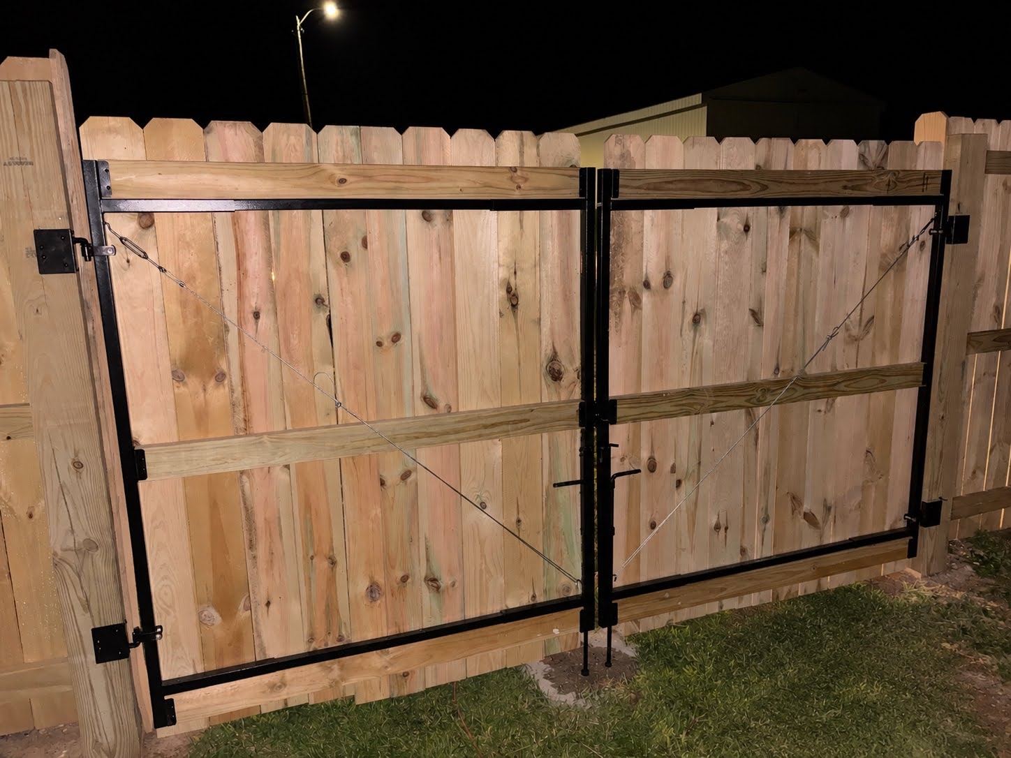 Double gate built on a welded black steel frame with a cable and turnbuckle brace, clad in matching pickets