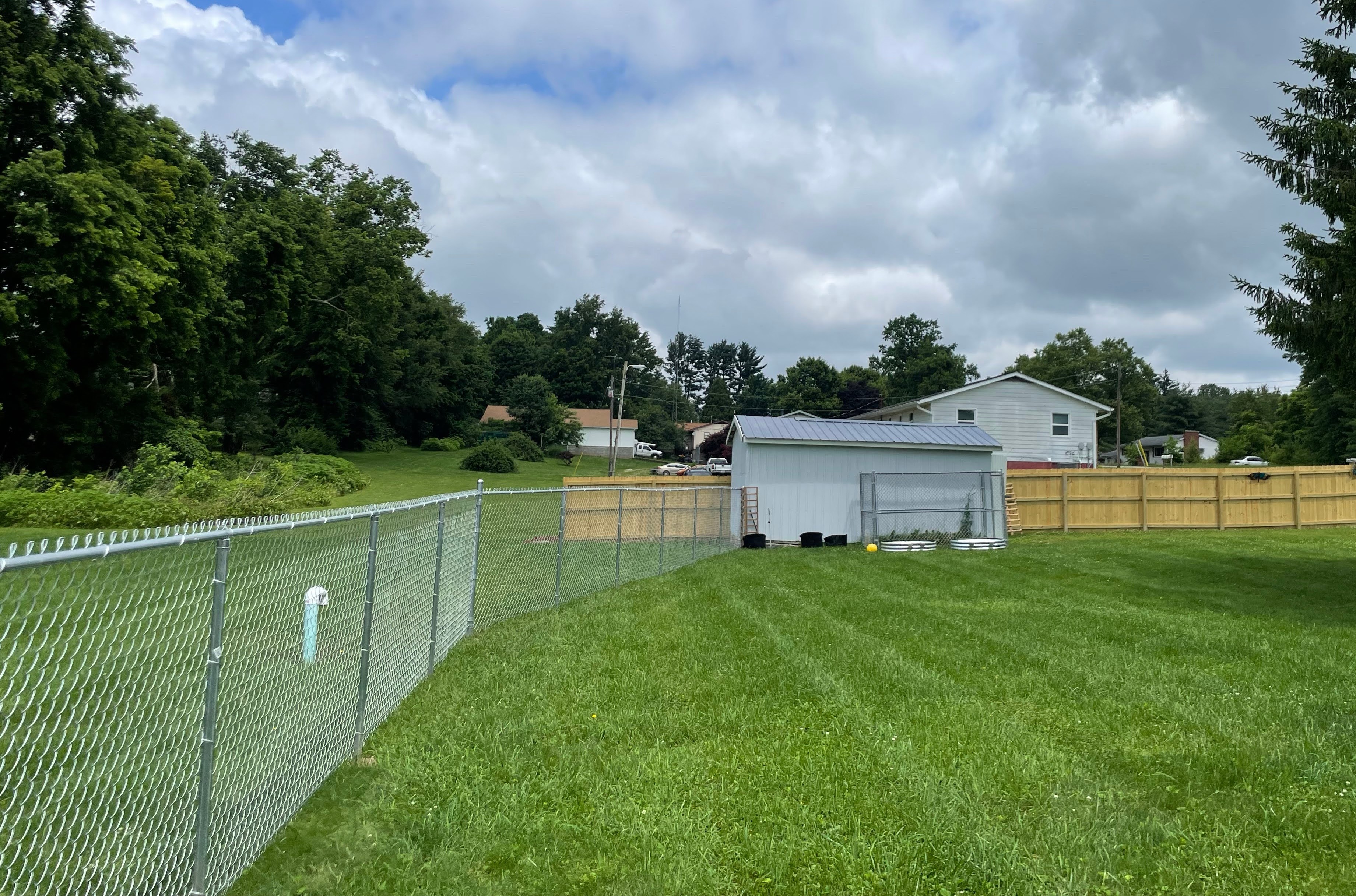 Galvanized chain-link fence enclosing a back yard, with a wood privacy fence along the far line